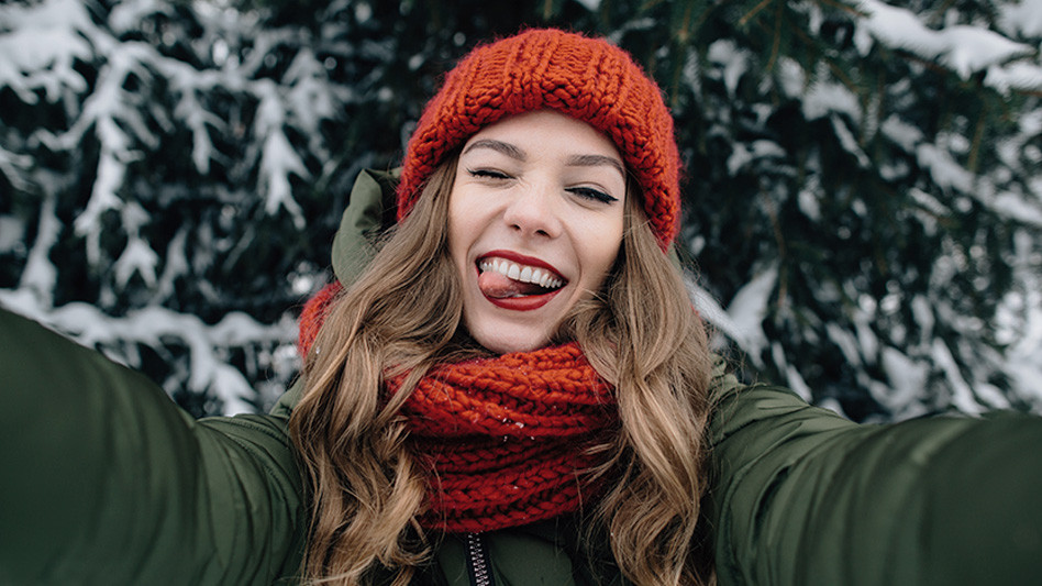 Kobieta uśmiechająca się do kamery robiąca zimowe selfie.